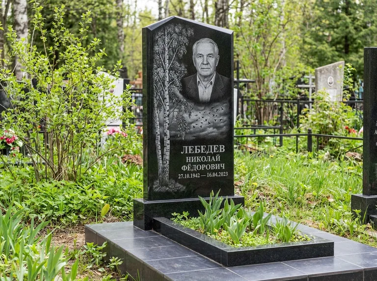 Памятник с гравировкой берёзы: вертикальная стела со скошенным верхом — берёза и стая птиц в небе, гранитный цоколь с тёмной плиткой, работа «Лебедев» в Челябинске
