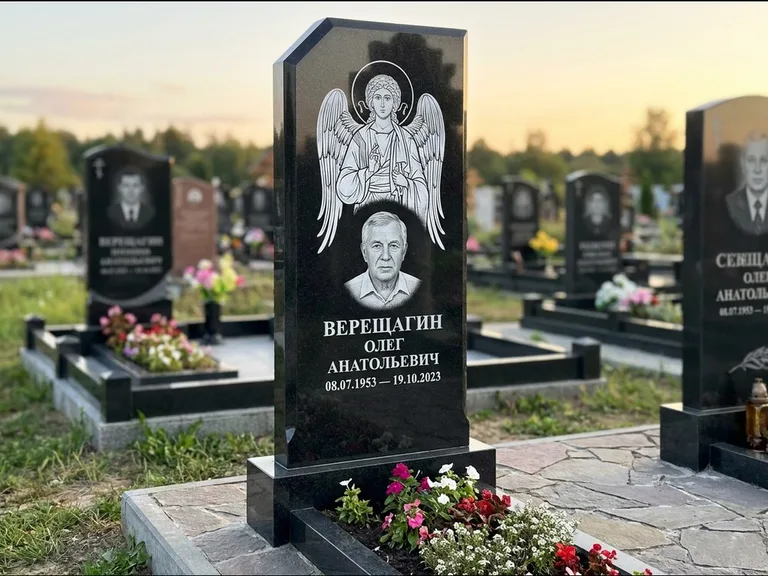 Памятник с гравировкой иконы: стела с резным навершием и нимбом в золоте — гравировка образа Спасителя, высокие разросшиеся туи полукругом, работа «Мельникова» в Челябинске