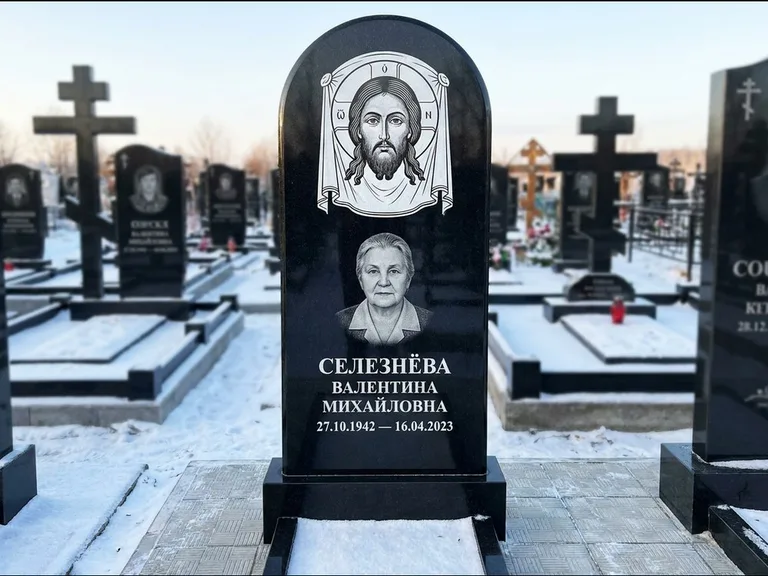 Памятник с гравировкой иконы: небольшая скромная одиночная стела с именной иконой — золочёный нимб на образе, аккуратный участок с газоном, работа «Ковалёв» в Челябинске