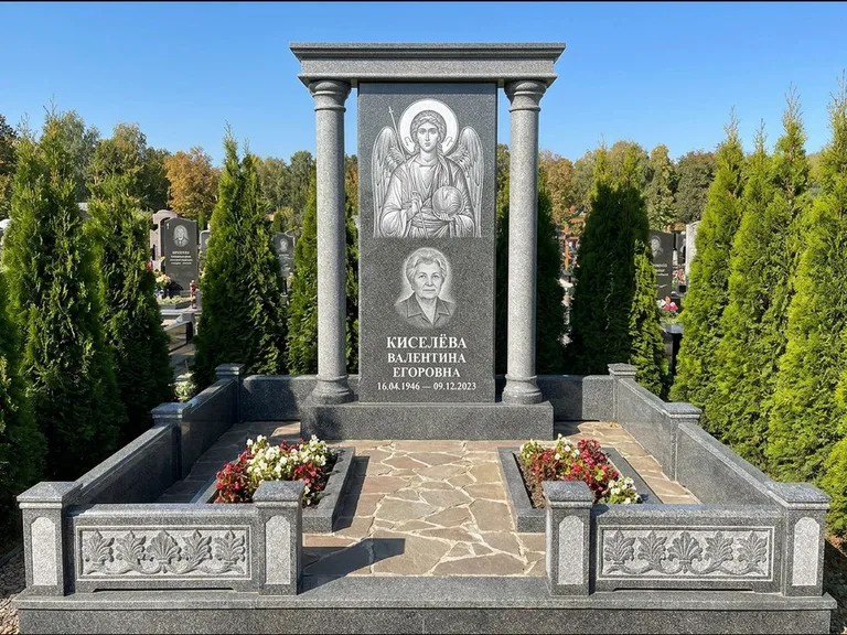 Памятник с гравировкой иконы: массивная стела с двускатным навершием-домиком — гравировка Николая Чудотворца, живая изгородь из туи, работа «Журавлёв» в Челябинске