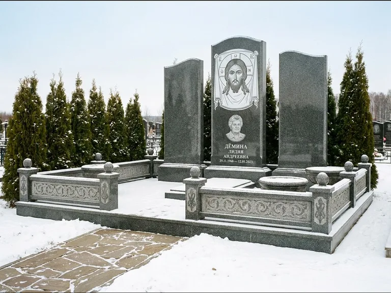 Памятник с гравировкой иконы: узкая вертикальная стела-пилон с ликом — икона в резной рамке-киоте, открытая лужайка без ограды, работа «Одинцов» в Челябинске
