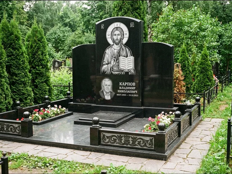 Памятник с гравировкой иконы: широкая панорамная стела с золочёным нимбом — гравировка образа Матроны Московской, цветник с белыми хризантемами, работа «Мельникова» в Челябинске