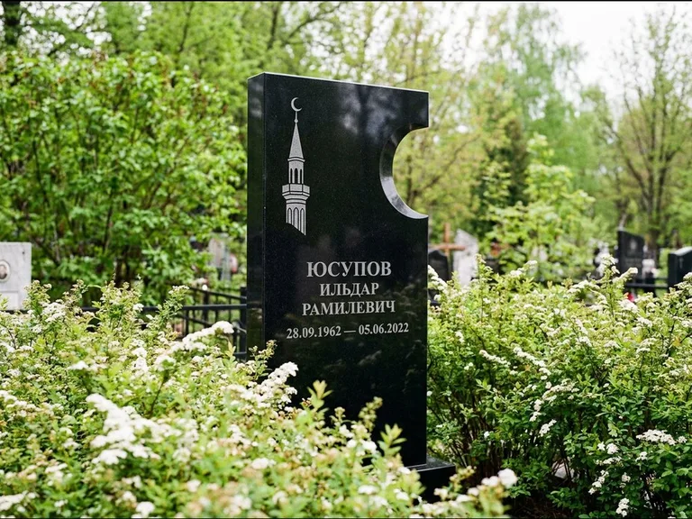 Мусульманский памятник с гравировкой мечети: стела с боковым вырезом в форме полумесяца — гравировка минарета с полумесяцем, низкие кусты спиреи в цвету, работа «Юсупов» в Челябинске