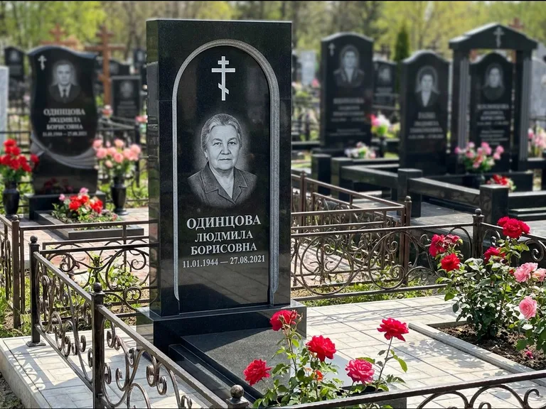 Памятник из чёрного гранита — скромная невысокая стела с крестом с терновым венцом, работа «Лаврентьева» в Челябинске